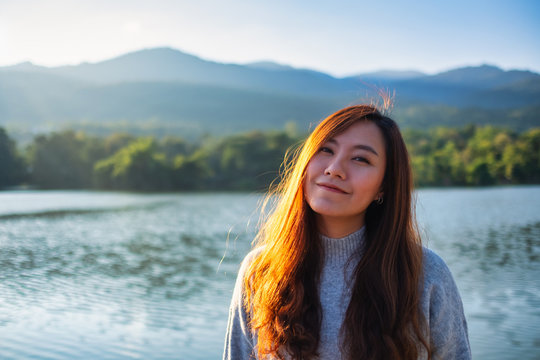 Portrait image of a beautiful asian woman standing in front of the lake and mountains before sunset