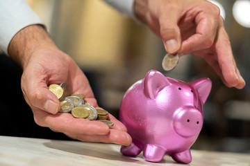 Male hands putting coins in a piggy bank