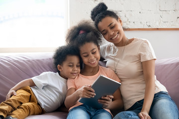 Happy biracial mom and little kids relax using tablet