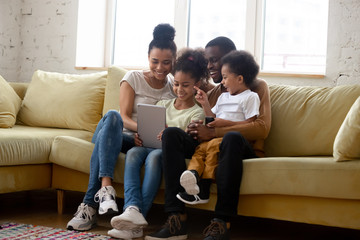 Overjoyed biracial family with kids have fun using tablet