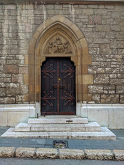 Fototapeta na wymiar Cathedral in Sarajevo entrance wooden door with ornaments and decorations and ancient historical stone wall around