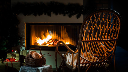 An empty rocking chair sways by the fireplace, next to a set for needlework. A place for winter holidays - obrazy, fototapety, plakaty