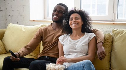 Overjoyed biracial couple have fun watching TV together