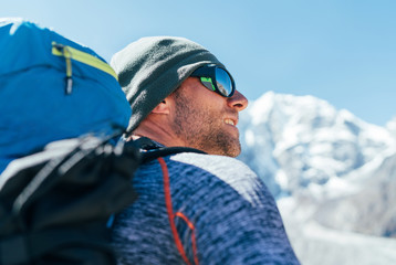 Portrait of unshaved Hiker man with backpack and UV protecting sunglasses on Taboche 6495m peakk...
