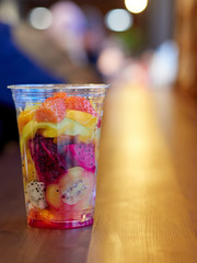 salad with mango, kiwi, strawberry, pineapple, pitaya, cactus fruit in a clear plastic Cup which is on a wooden table. health food. organic food. exotic fruit. close up.