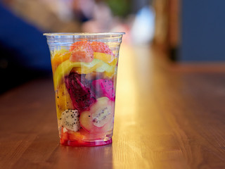 salad with mango, kiwi, strawberry, pineapple, pitaya, cactus fruit in a clear plastic Cup which is on a wooden table. health food. organic food. exotic fruit. close up.