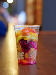 salad with mango, kiwi, strawberry, pineapple, pitaya, cactus fruit in a clear plastic Cup which is on a wooden table. health food. organic food. exotic fruit. close up.