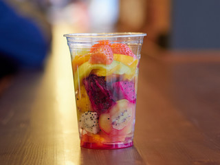 salad with mango, kiwi, strawberry, pineapple, pitaya, cactus fruit in a clear plastic Cup which is on a wooden table. health food. organic food. exotic fruit. close up.