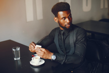 Fototapeta na wymiar A young and handsome dark-skinned boy in a black suit sitting in a cafe
