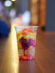 salad with mango, kiwi, strawberry, pineapple, pitaya, cactus fruit in a clear plastic Cup which is on a wooden table. health food. organic food. exotic fruit. close up.