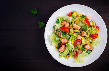 Salad with grilled salmon, lettuce, avocado, tomatoes and corn on a white bowl. Paleo diet. Top view, copy space