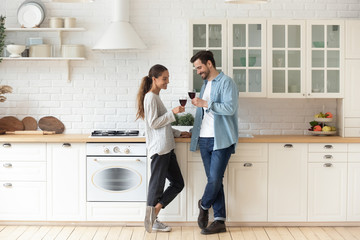 Romantic affectionate young couple drinking wine standing in modern kitchen