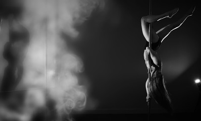 The dancer on the pylon in the studio. Girl doing exercises on a sports equipment.