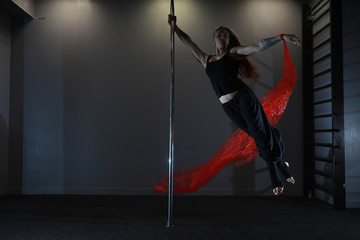 Obraz na płótnie Canvas The dancer on the pylon in the studio. Girl doing exercises on a sports equipment.