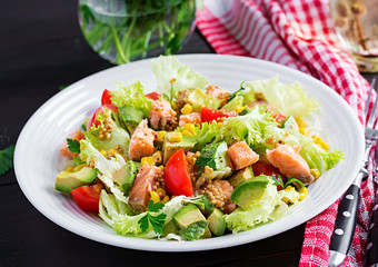 Salad with grilled salmon, lettuce, avocado, tomatoes and corn on a white bowl. Paleo diet.