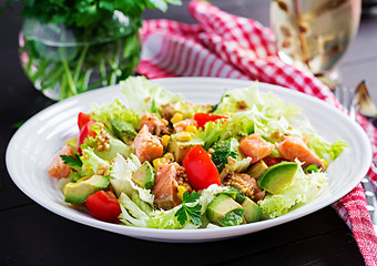 Salad with grilled salmon, lettuce, avocado, tomatoes and corn on a white bowl. Paleo diet.
