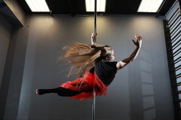 The dancer on the pylon in the studio. Girl doing exercises on a sports equipment.