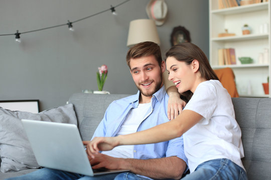 Young couple doing some online shopping at home, using a laptop on the sofa.