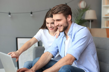 Fototapeta premium Young couple doing some online shopping at home, using a laptop on the sofa.