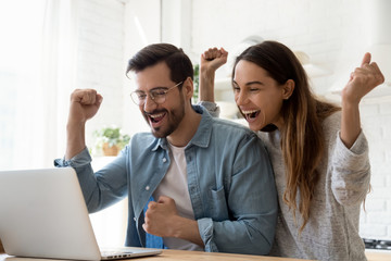 Excited young couple using laptop celebrate online win together