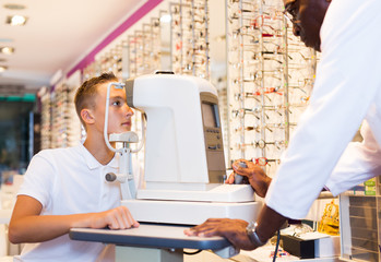 Optician testing teenager eyesight on refractometer