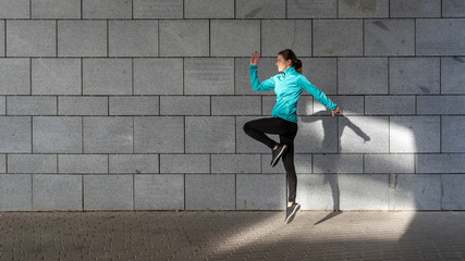Young adult sporty girl  jumping up against wall outdoor