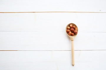 Hazelnuts in spoon on white wooden table with clipping path