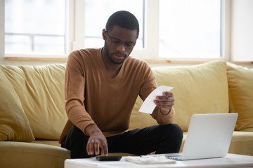 Concentrated biracial man calculating household expenses at home