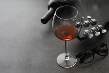 Guitar and high glass with red wine on a stone background.