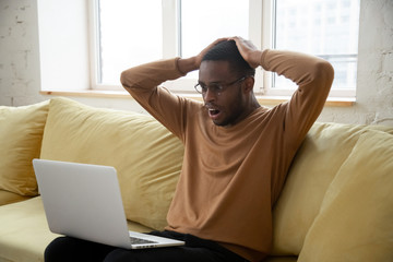 African American man shocked by online news on laptop