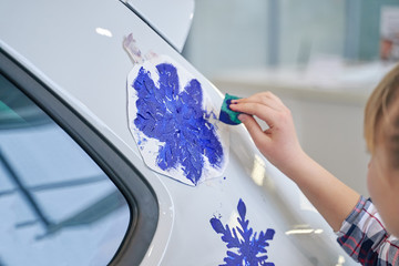 child draws snowflakes on a car using a stencil