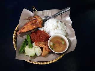 Popular food among Malaysian called (Nasi Ayam Penyet) rice served with fried chiken, fermented soybean call Tempe, spicy sauce, vegetables and hot sup. Original dish from Indonisia. Black background.
