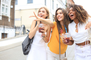 Three trendy cool hipster girls, friends drink cocktail in urban city background.