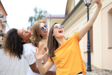 Three cute young girls friends having fun together, taking a selfie at the city.