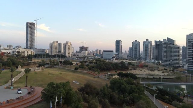 Aerial flying over an Ashdod city and Ashdod-Yam Park with cloudy sunset sky, buildings, sea and coast at the background. View from above of Ashdod, Israel
