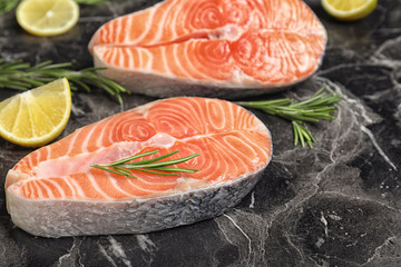 Fresh raw salmon, rosemary and lemon on black marble table. Fish delicacy