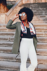 Fashionable girl in a summer city. Black lady in a green jacket. Woman in a red scarf. Famale with sunglasses