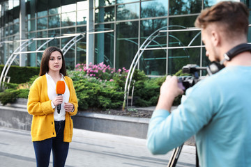 Young journalist and video operator working on city street