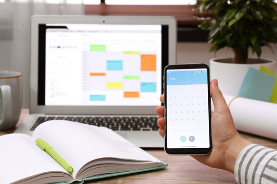 Woman holding smartphone with calendar app at table, closeup