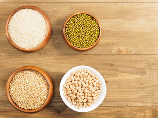 Rice, oat, chick pea, green gram in cups on brown wooden background. Indian cuisine, ayurveda, naturopathy, modern apothecary concept