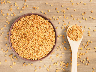 Fenugreek in clay plate and spoon on a brown wooden background. Indian cuisine, ayurveda, naturopathy, modern apothecary concept