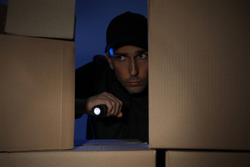Security guard with flashlight looking through pile of cardboard boxes in dark room