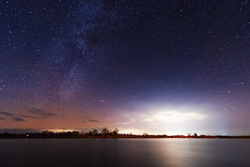 A magical starry night on the river bank with a milky way in the sky and falling stars in the winter.