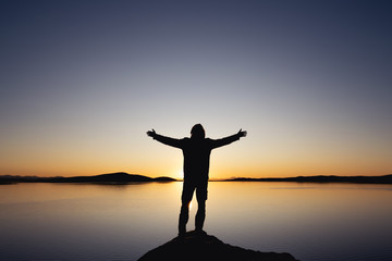 Fototapeta na wymiar Silhouette with raised arms against sunset lake