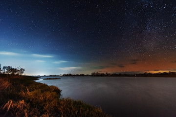 A magical starry night on the river bank with a milky way in the sky and falling stars in the winter.