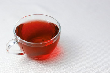 red cup of tea with hibiscus on the table on a white tablecloth. Invigorating tea