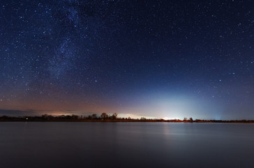 A magical starry night on the river bank with a milky way in the sky and falling stars in the winter.