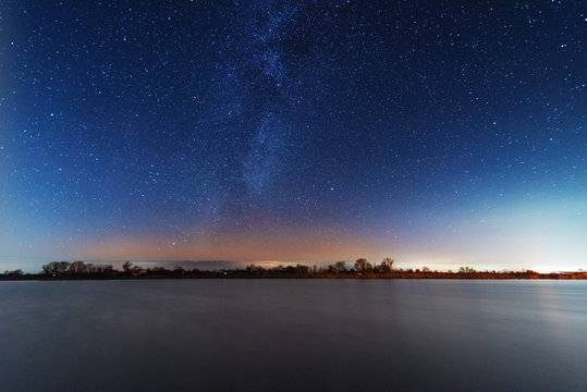 A magical starry night on the river bank with a milky way in the sky and falling stars in the winter.