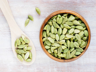Spice Green cardamom (Elettaria cardamomum) in a wooden cup and spoon on a white wooden background