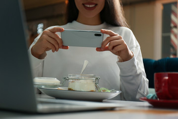 Blogger taking picture of dessert at table in cafe, closeup
